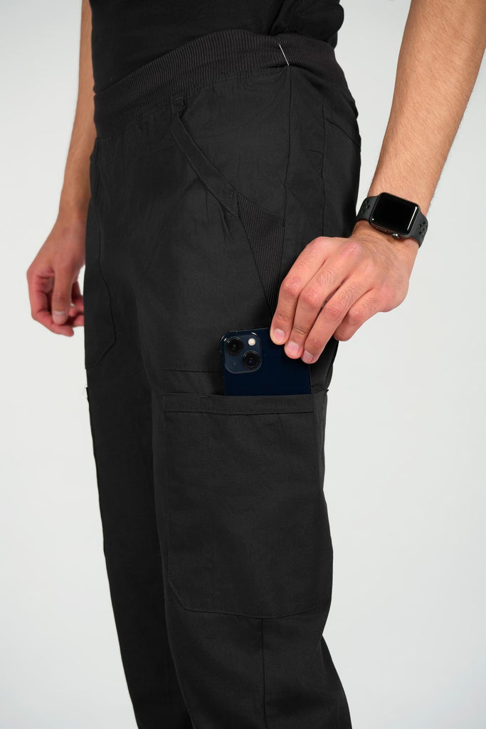 Men's 6-Pocket Elastic Scrub Pant in black closeup on model putting phone into pocket