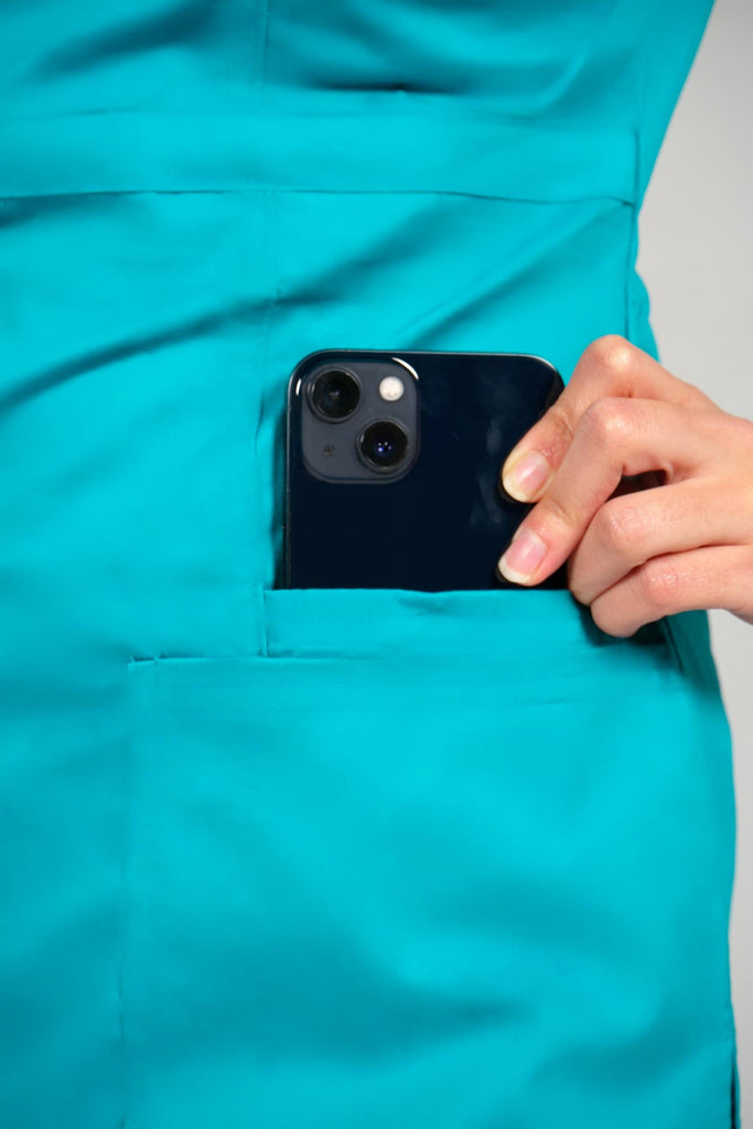 Women's 4-Pocket Curved V-Neck Scrub Top in Teal model pulling phone out of bottom pocket