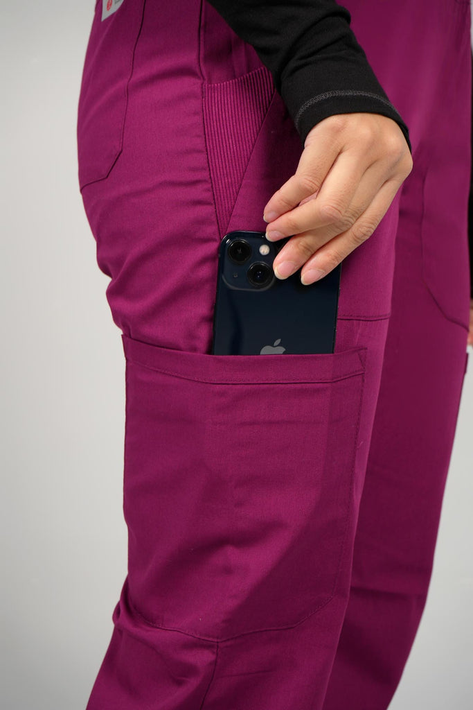 Women's 6-Pocket Elastic Scrub Pant in Wine closeup on model putting phone into pocket