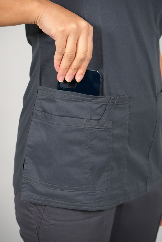 Women's Tailored 4-Pocket V-Neck Scrub Top in Charcoal model putting phone into pocket