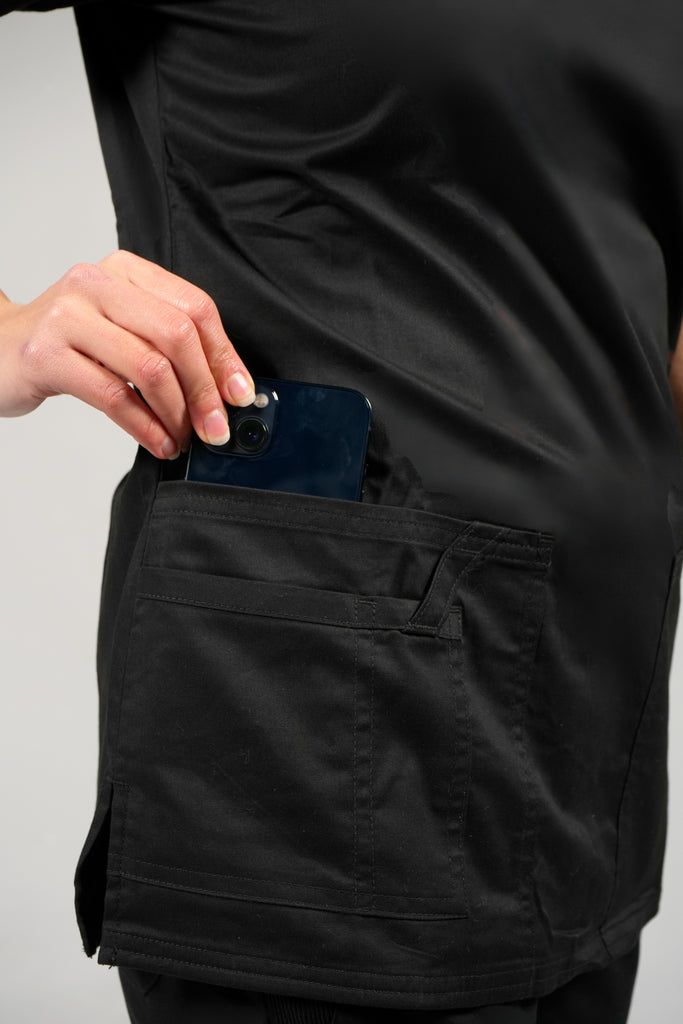 Women's Tailored 4-Pocket V-Neck Scrub Top in black model putting phone into pocket