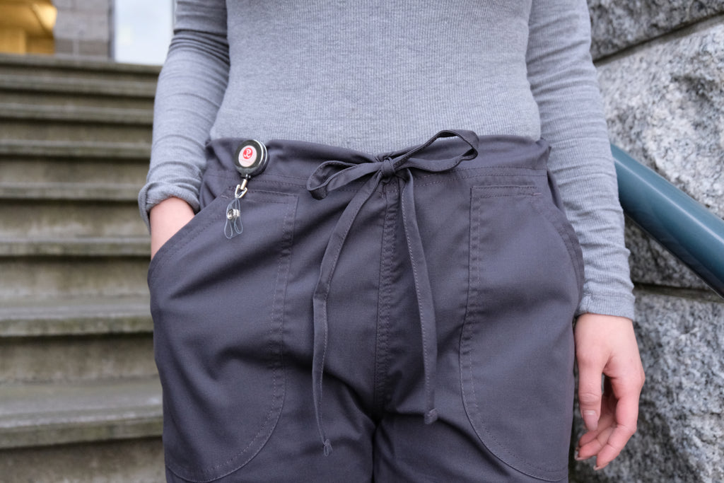 Women's 4-Pocket Scrub Pants in charcoal closeup on drawstring, pockets and id badge reel on model
